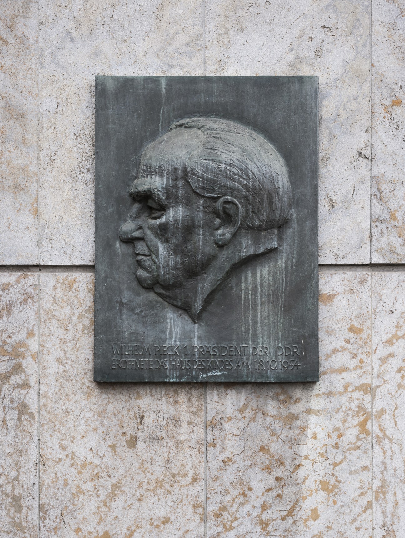 Black stone plaque depicting Wilhelm Pieck, first president of the GDR, mounted on a building facade.