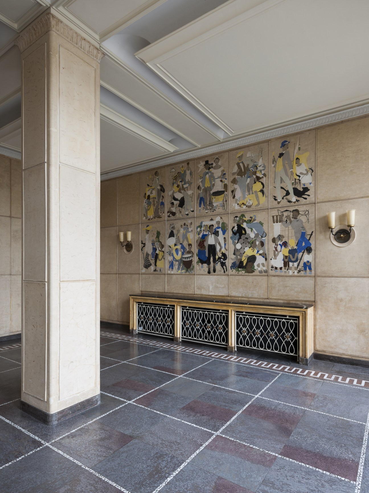 Foyer with decorative mosaics showing figures in blue and yellow on beige wall panels above storage cabinets.