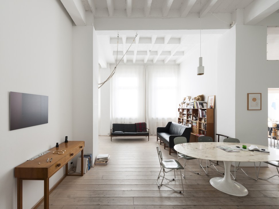 Minimalist apartment interior with white walls, wooden floor, mid-century furniture, and large windows overlooking Karl-Marx-Allee in Berlin's Henselmann Tower.