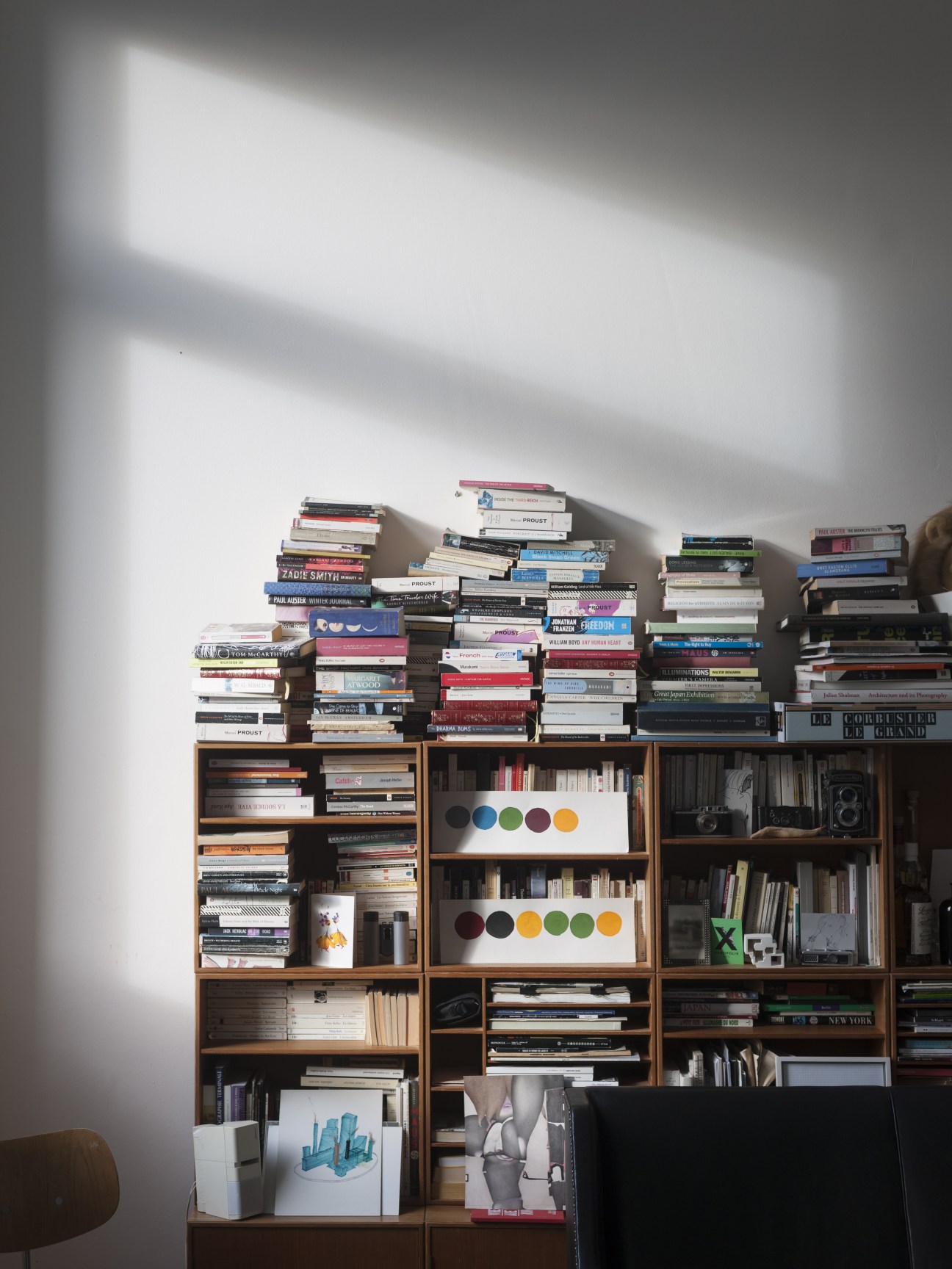 Wooden shelving unit stacked with books, magazines, and decorative objects with colorful circular art pieces displayed on white shelves.