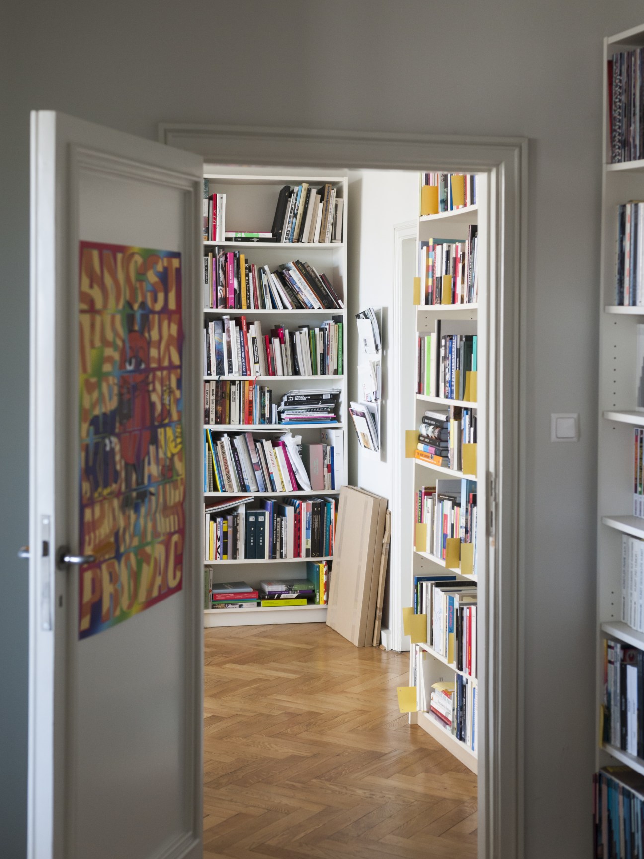 Open doorway leading to shelving filled with stacked art theory magazines and books in white built-in cabinets.