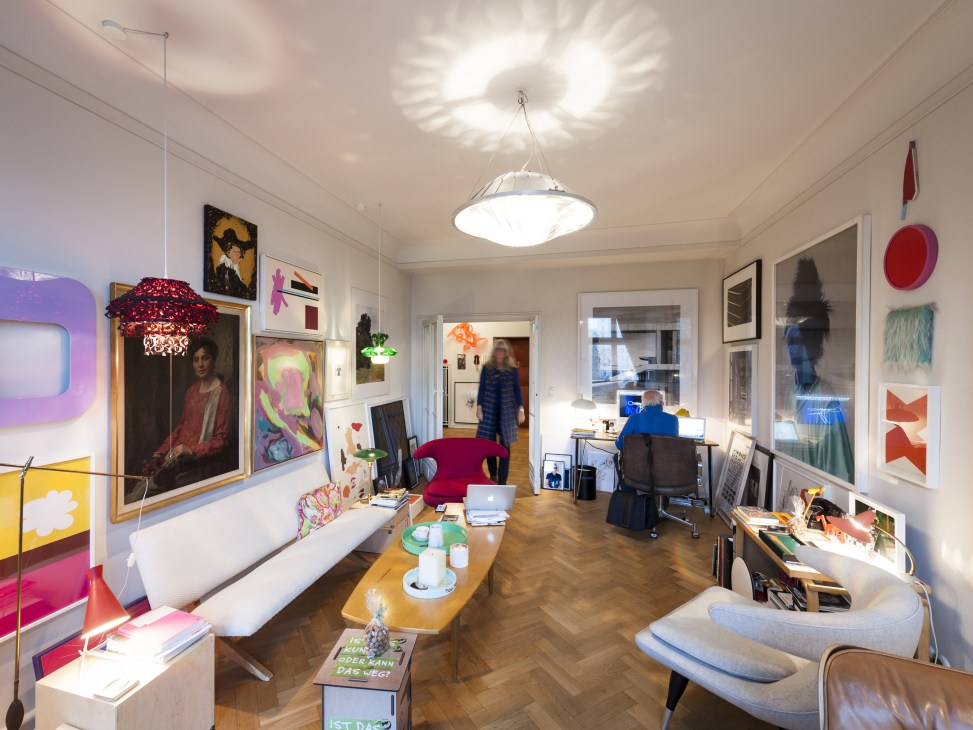 Apartment interior with colorful artworks, red pendant light, and residents working at desks