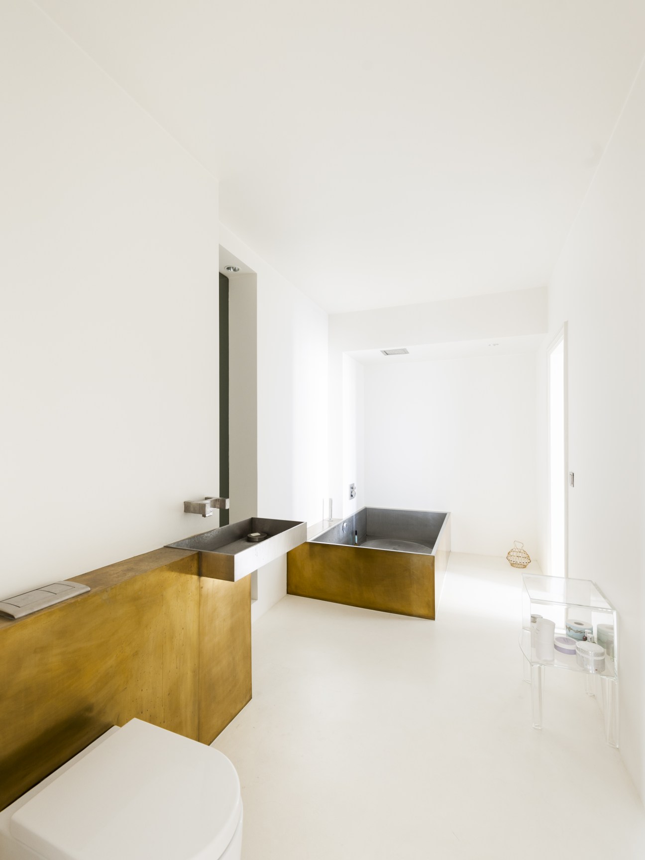 Modern minimalist bathroom with brass and steel fixtures, white walls, and clean lines in the Henselmann Tower.