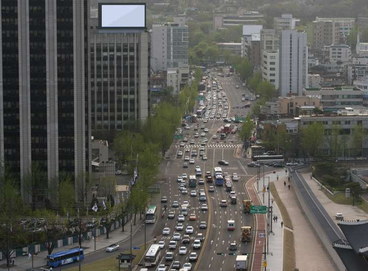 Aerial view of Seoul street with heavy traffic, pedestrian crossings, and a mountain in the background.