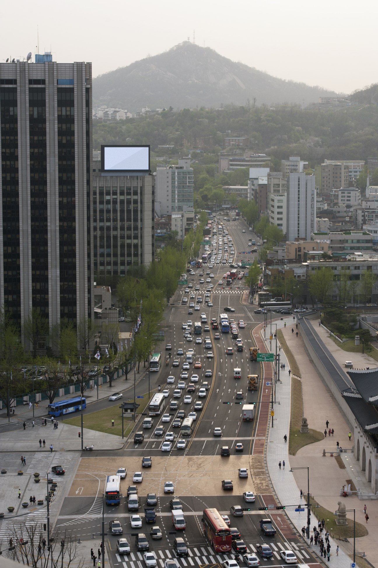 Aerial view of Seoul street with heavy traffic, pedestrian crossings, and a mountain in the background.