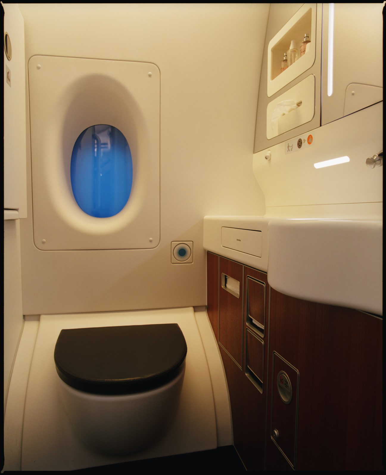 Spacious Airbus A380 aircraft lavatory with blue vacuum toilet, cream-colored walls, illuminated mirror cabinet, and wooden storage panels.