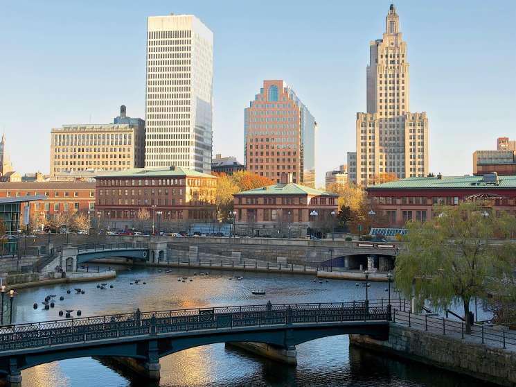 Providence skyline with historic buildings, bridges spanning a river, and autumn foliage along the waterfront.