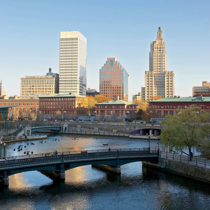 Providence skyline with historic buildings, bridges spanning a river, and autumn foliage along the waterfront.