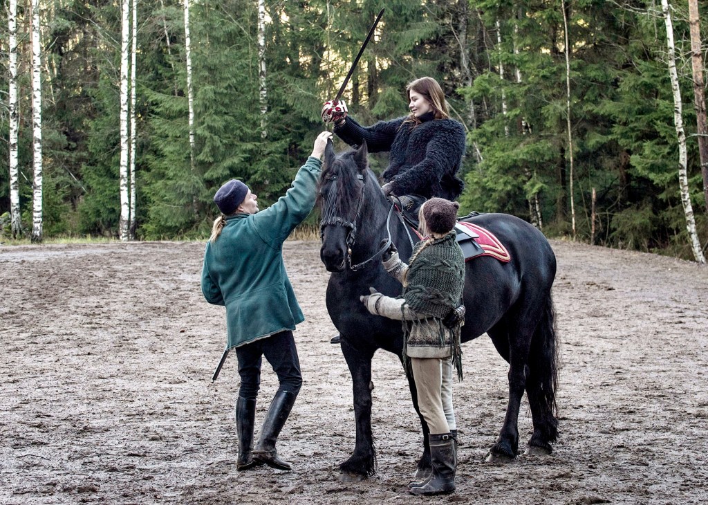 Actress Malin Buska rehearsing a scene on horseback for the film 'The Girl King' in a forest clearing.