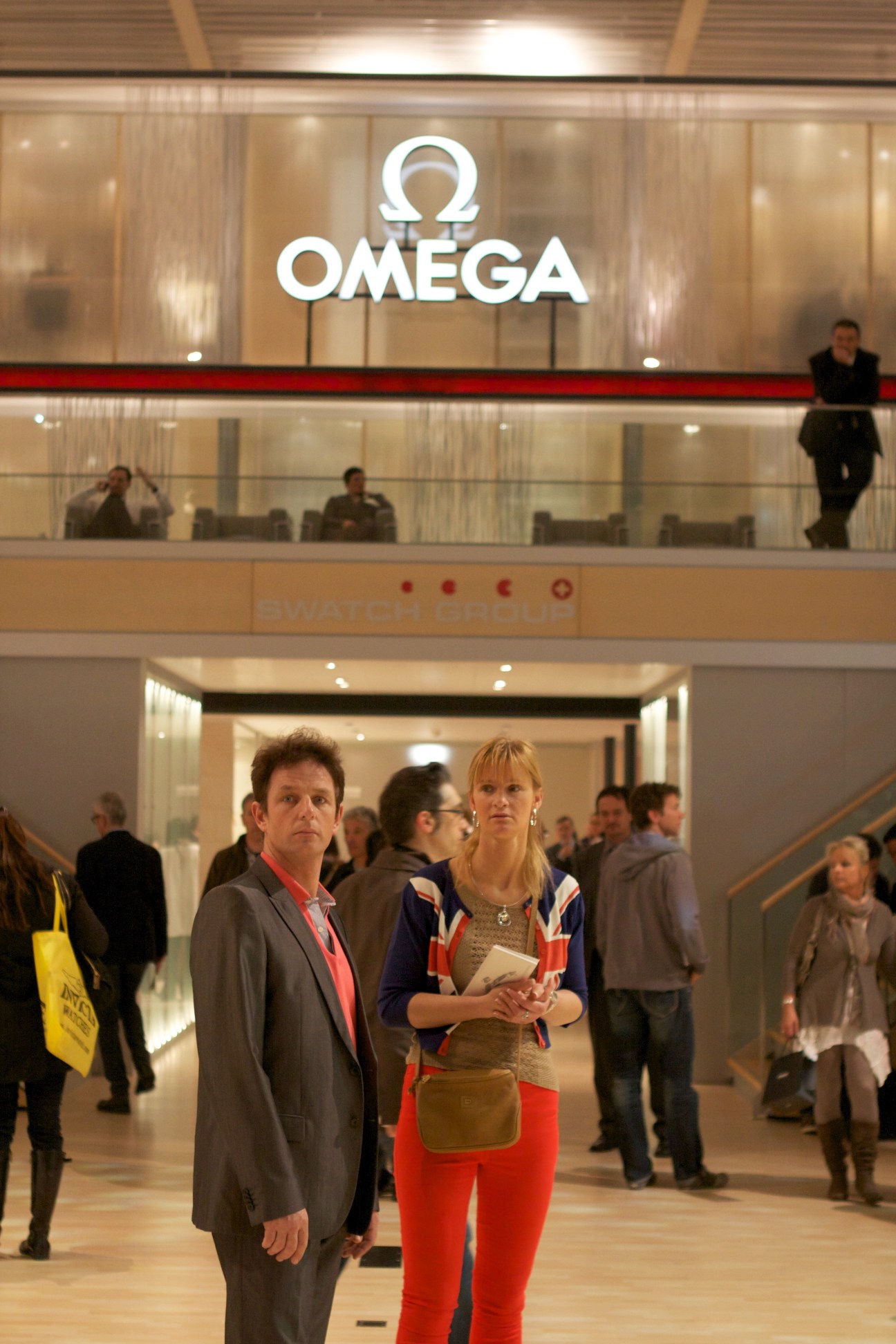 Visitors browse the Omega stand at Basel watch fair with illuminated logo and multi-level gallery space.