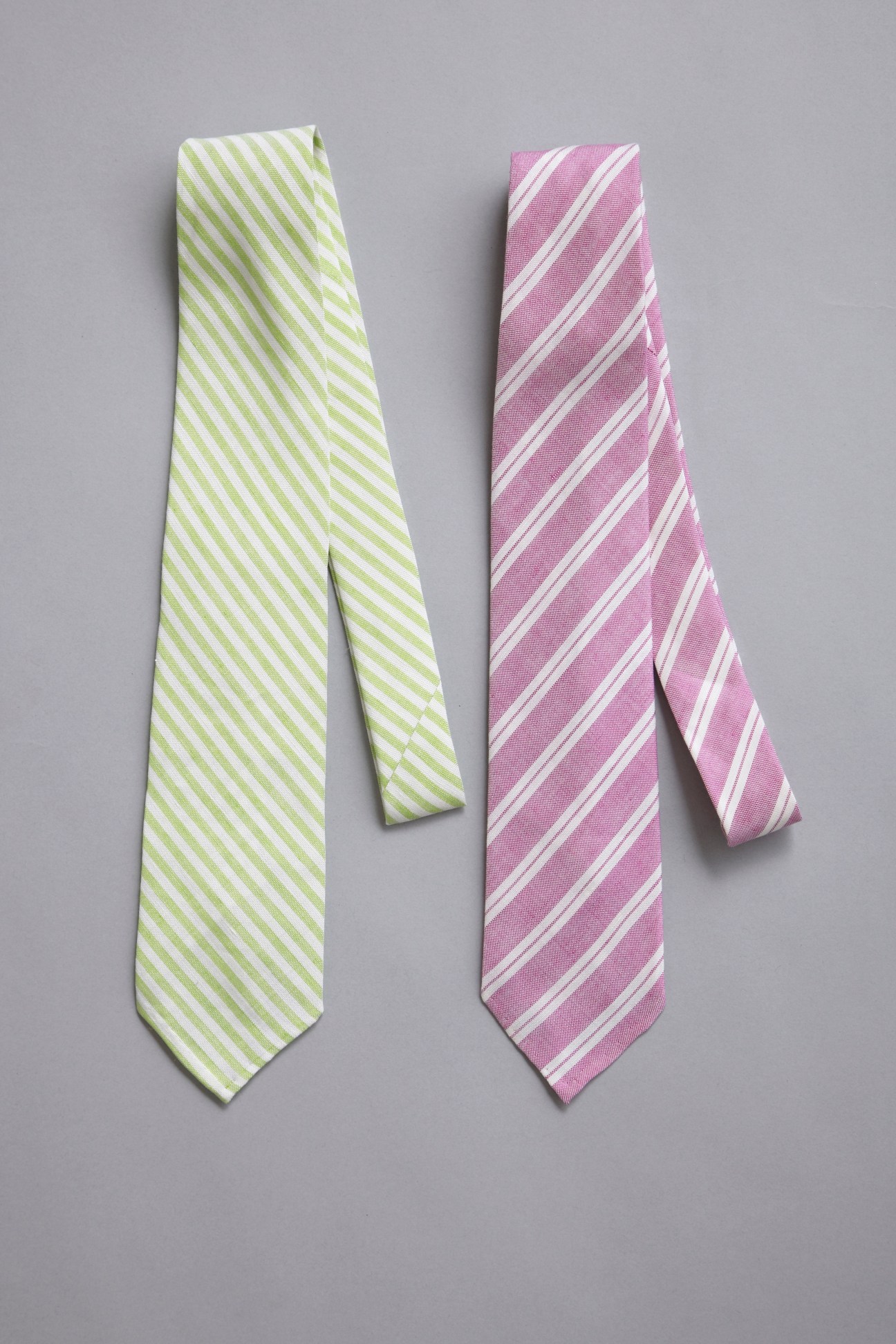 Two striped neckties, one lime green and one pink with white diagonal stripes, displayed on a gray background.