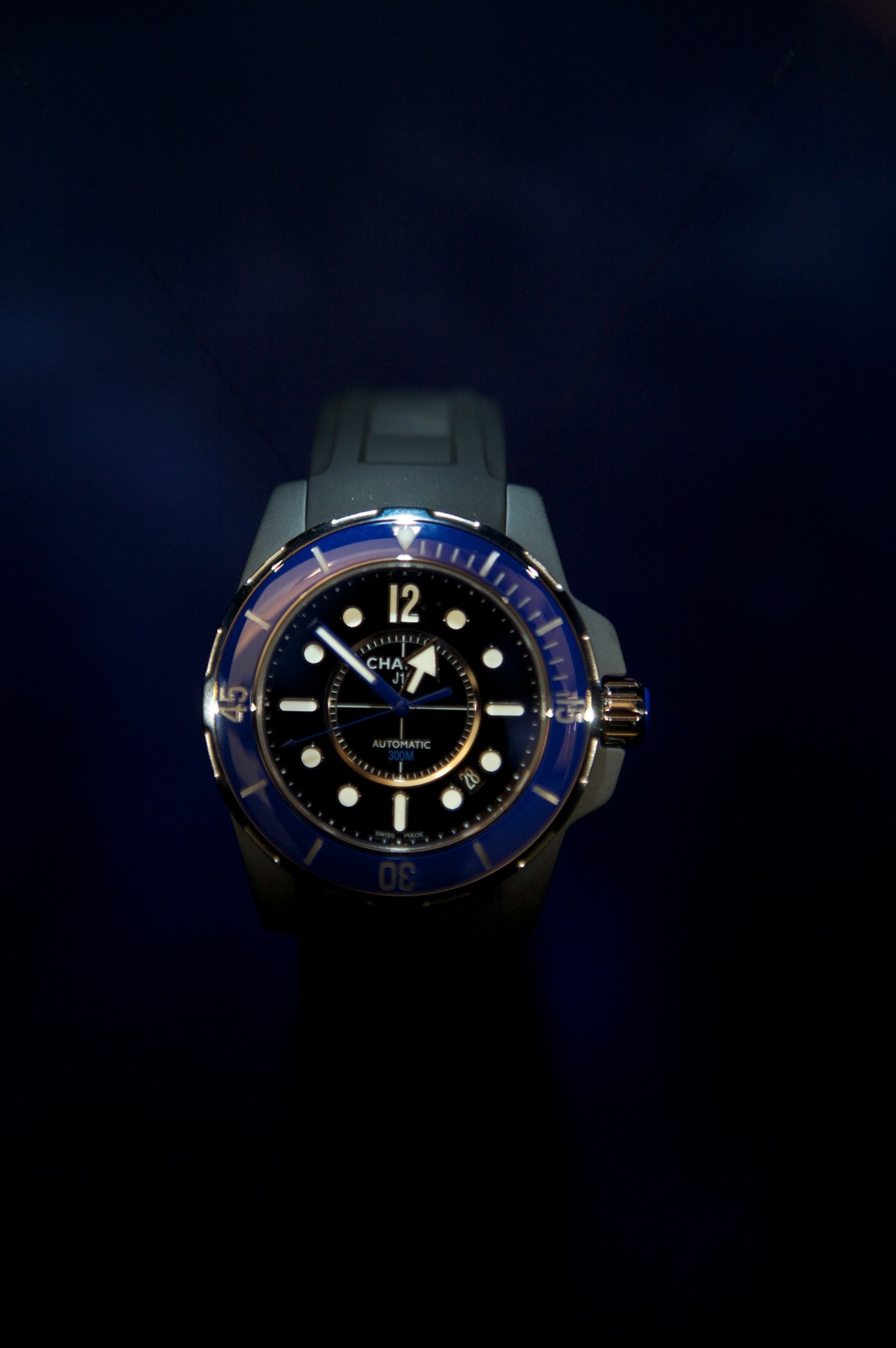Chanel J12 Marine watch with black dial, blue bezel, and black rubber strap on dark background.