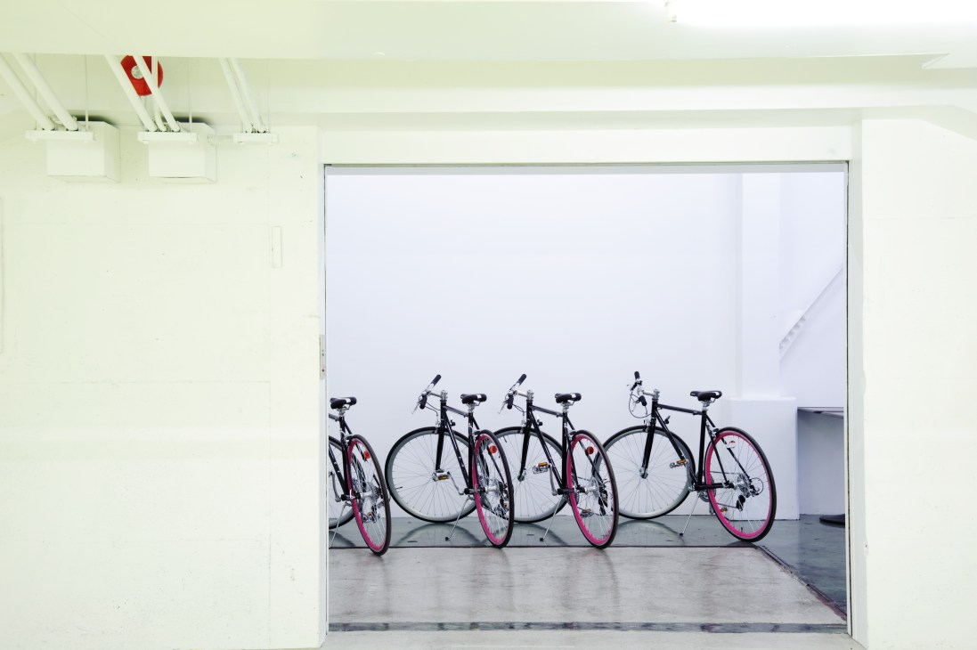 Five Osso bicycles with black frames and pink accents lined up in a bright white storage space at Tabloid.