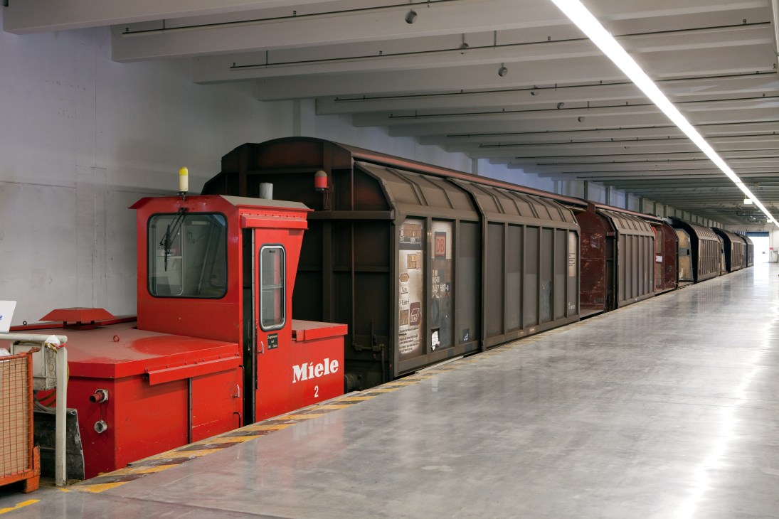 Miele's red and black freight train with numbered locomotive inside a factory warehouse.