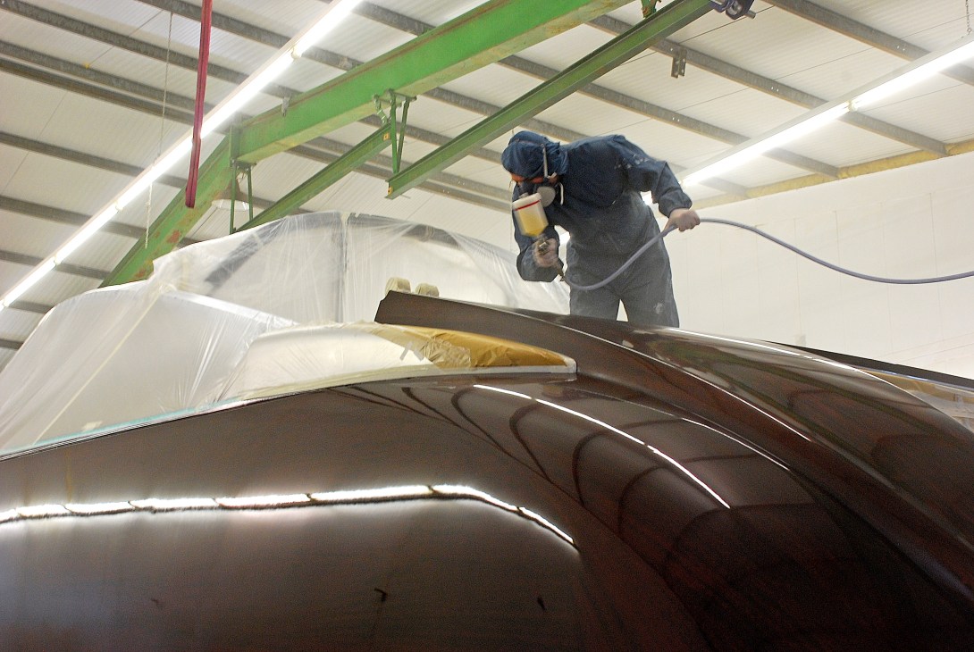 Craftsman applying hi-tech varnish to the mahogany hull of an Aguti yacht in a shipyard workshop.