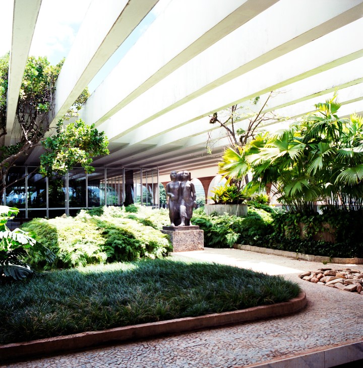Interior garden courtyard with bronze sculpture and lush vegetation under geometric skylights.