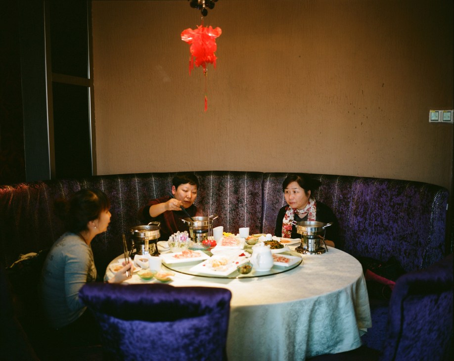 Three people dining at a round table in a restaurant with a red lantern hanging from the ceiling in Heihe, China.