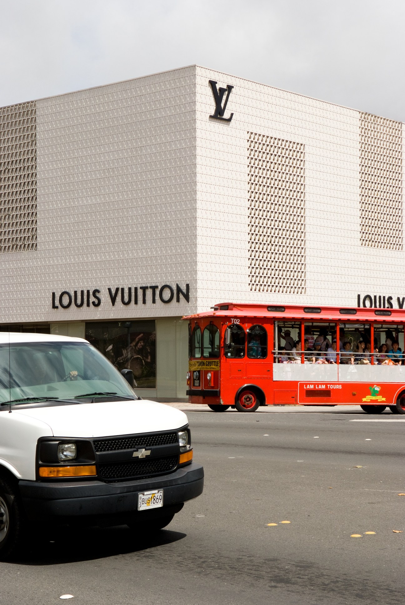 Louis Vuitton store in Guam with white latticed facade and large LV logo, red tour bus passing in front.