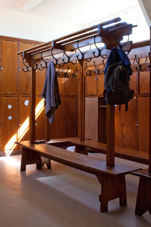 Interior of a wooden changing room with lockers, benches, and hooks for storing clothes and towels.