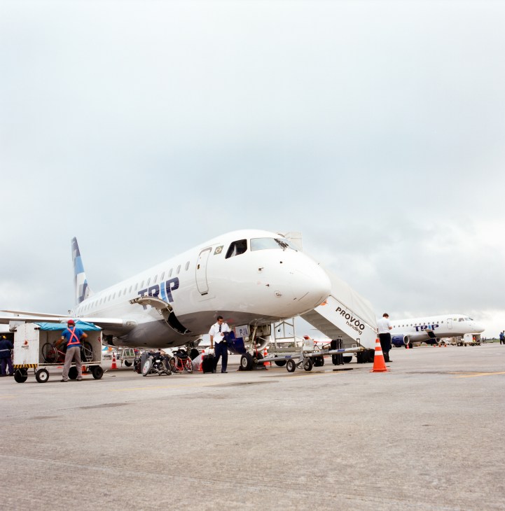 A Trip Linhas Aéreas aircraft parked at an airport terminal with ground crew and service vehicles.