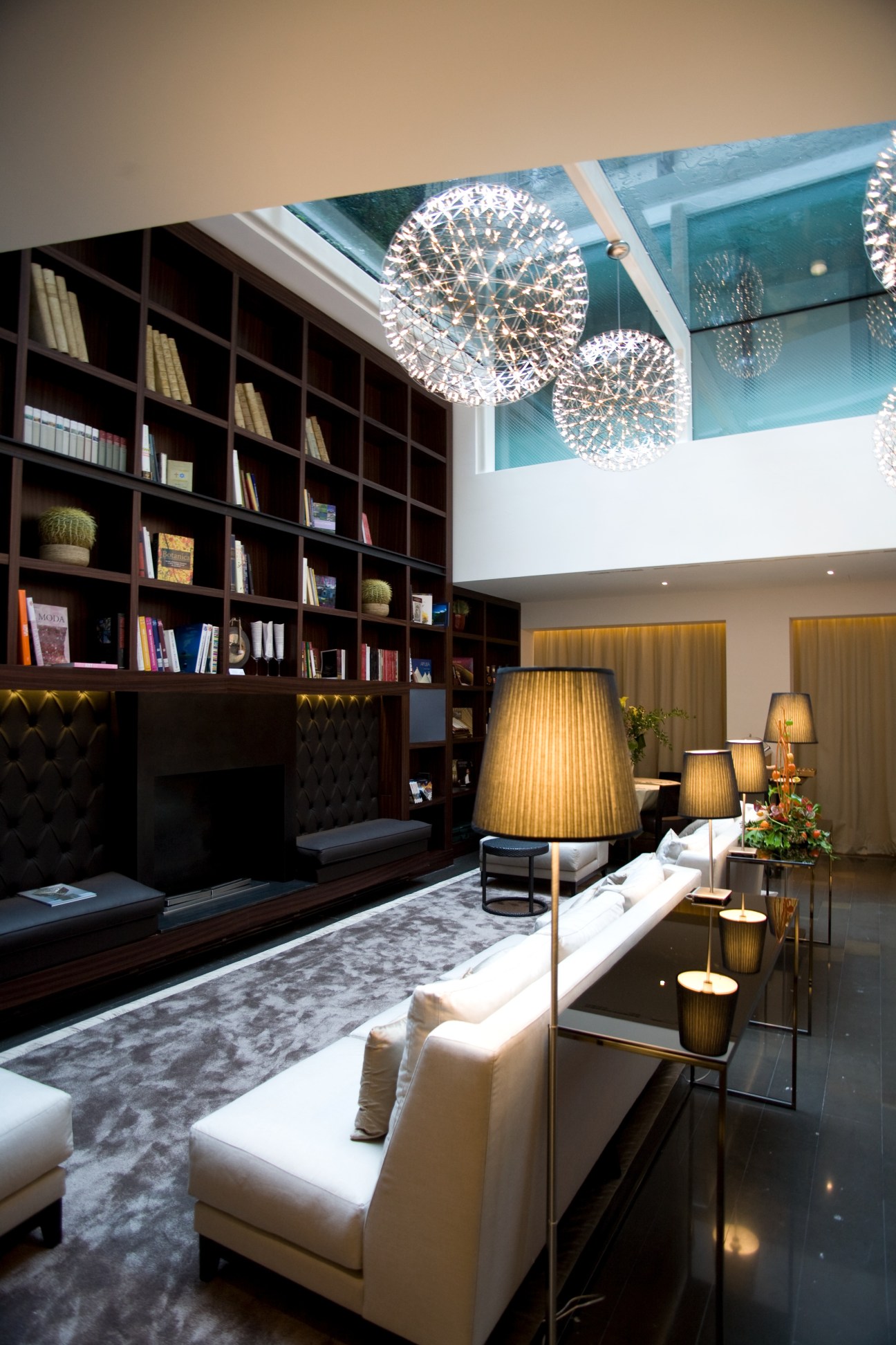 Modern hotel suite interior with built-in bookshelves, white seating, spherical pendant lights, and high ceiling at Hotel Milano Scala.