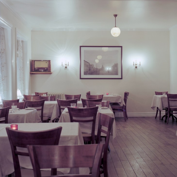 Interior of Ravda Husid restaurant with purple chairs, white tablecloths, and vintage décor on cream walls.