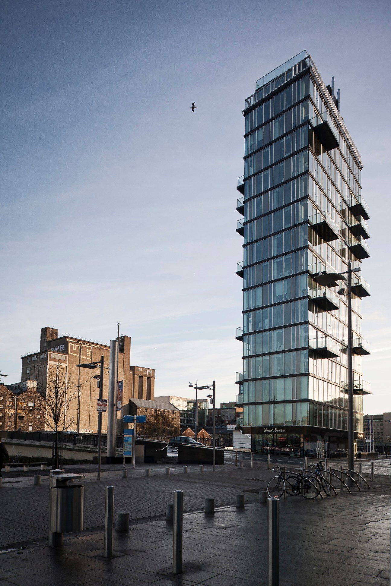 Modern glass and steel tower building at Grand Canal dock in Dublin with historic warehouses nearby.