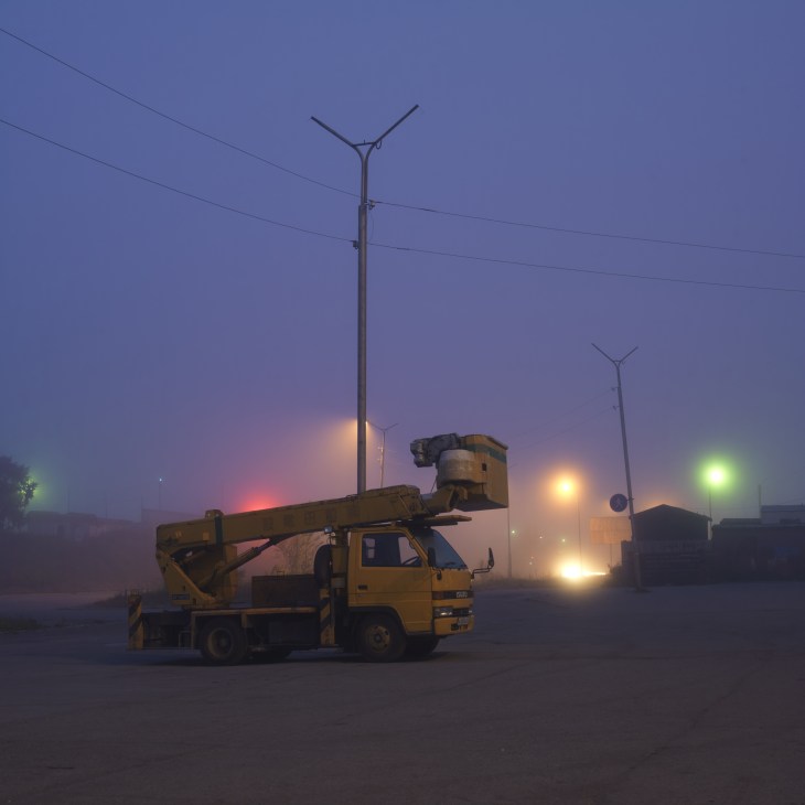Yellow utility truck with raised crane arm on industrial lot at dusk in Petropavlovsk, Kamchatka.