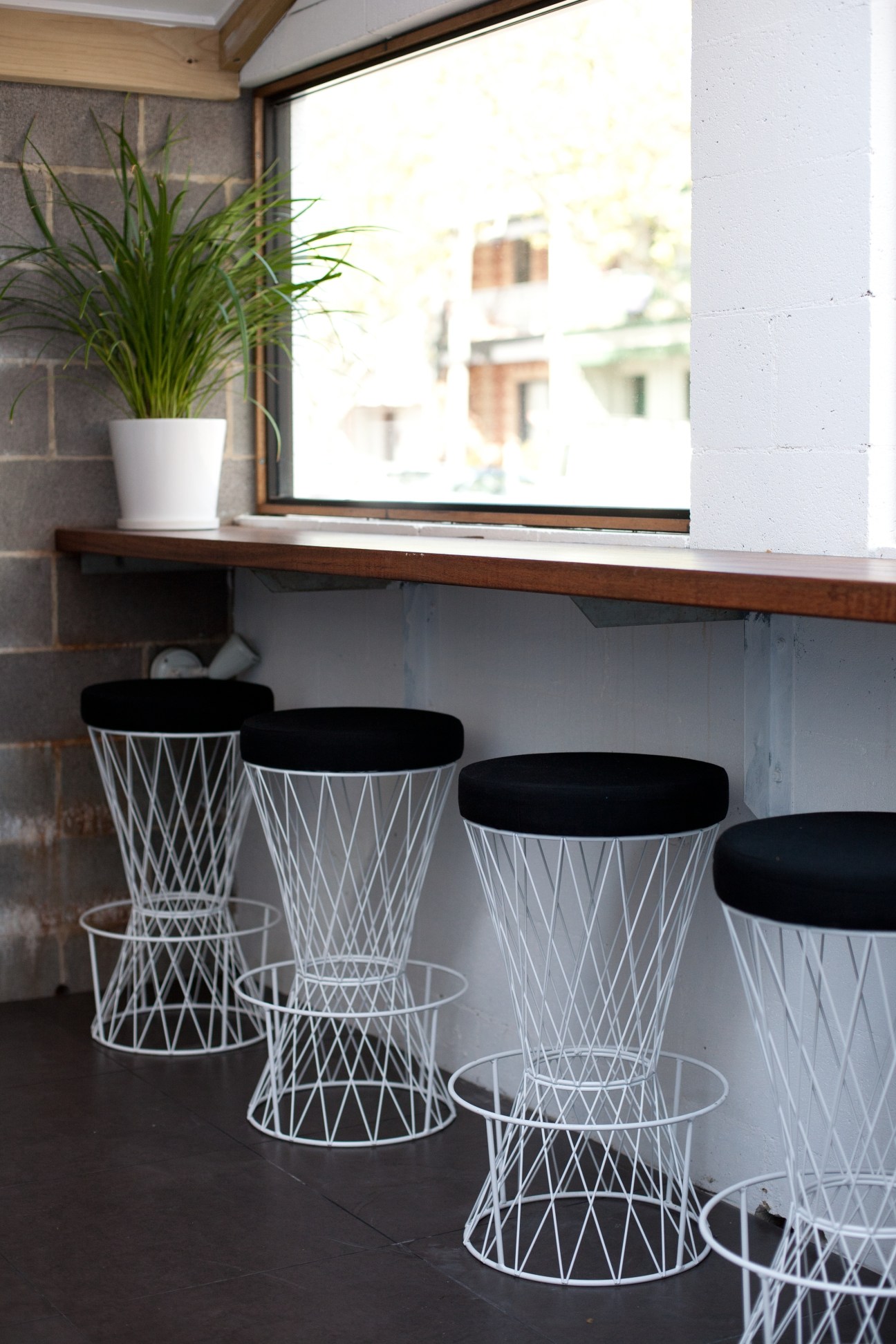 Modern bar seating with white wire-frame stools and black cushions under a wooden counter facing a window.
