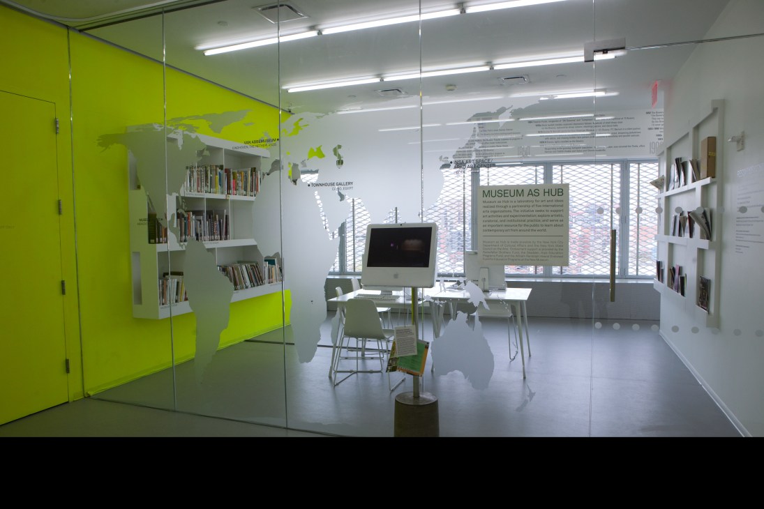 New Museum resource centre with bright yellow storage cabinets, glass partitions, bookshelves and computer workstation.