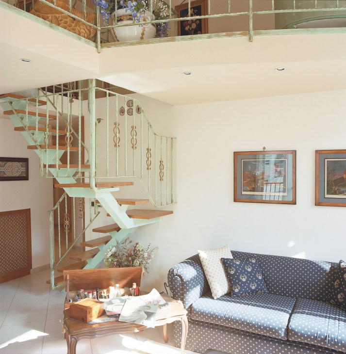 Contemporary apartment interior with mint green spiral staircase, cream walls, and patterned sofa.