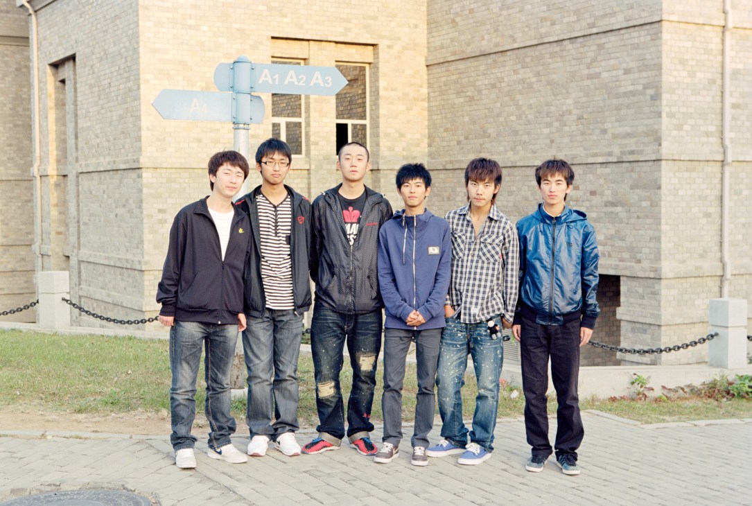 Six male students standing in front of a grey brick building at Neusoft Information Institute.
