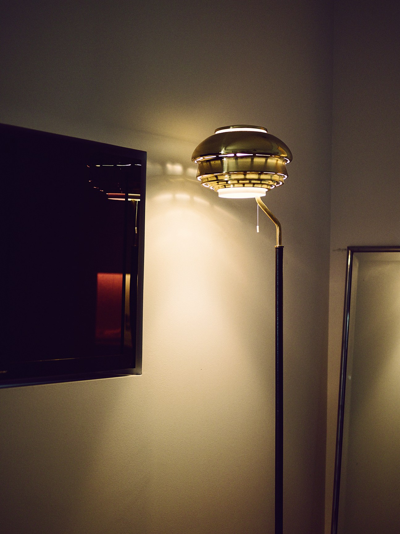 A808 brass floor lamp by Alvar Aalto for Artek with tiered dome shade and curved brass stem against white wall.