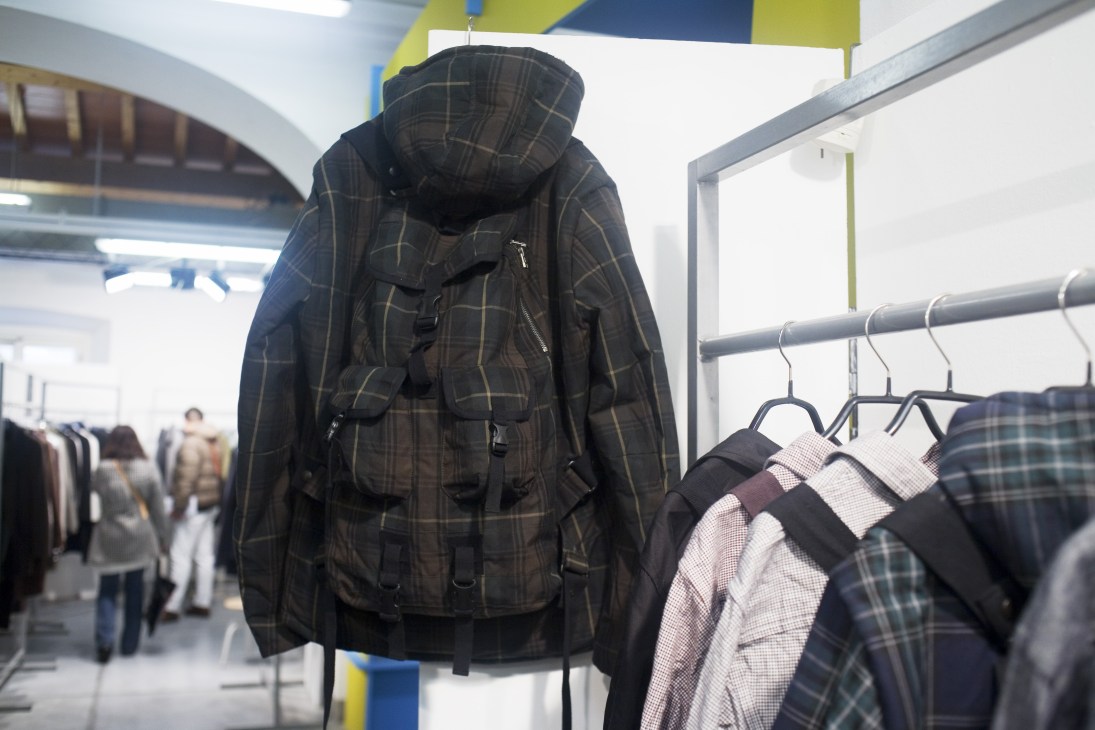 Plaid jacket with integrated backpack straps displayed at Pitti Uomo menswear trade show