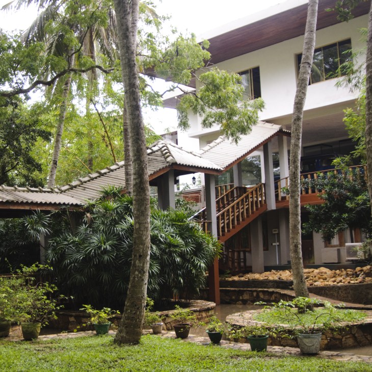 Peacock Beach Hotel in Hambantota, a modern multi-story building with white walls, wooden railings and tropical vegetation.