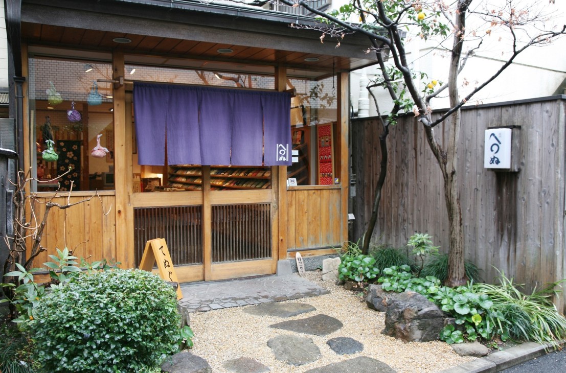 Traditional Japanese wooden storefront with purple noren curtain and moss-covered entrance at Kamawanu craft shop in Tokyo.