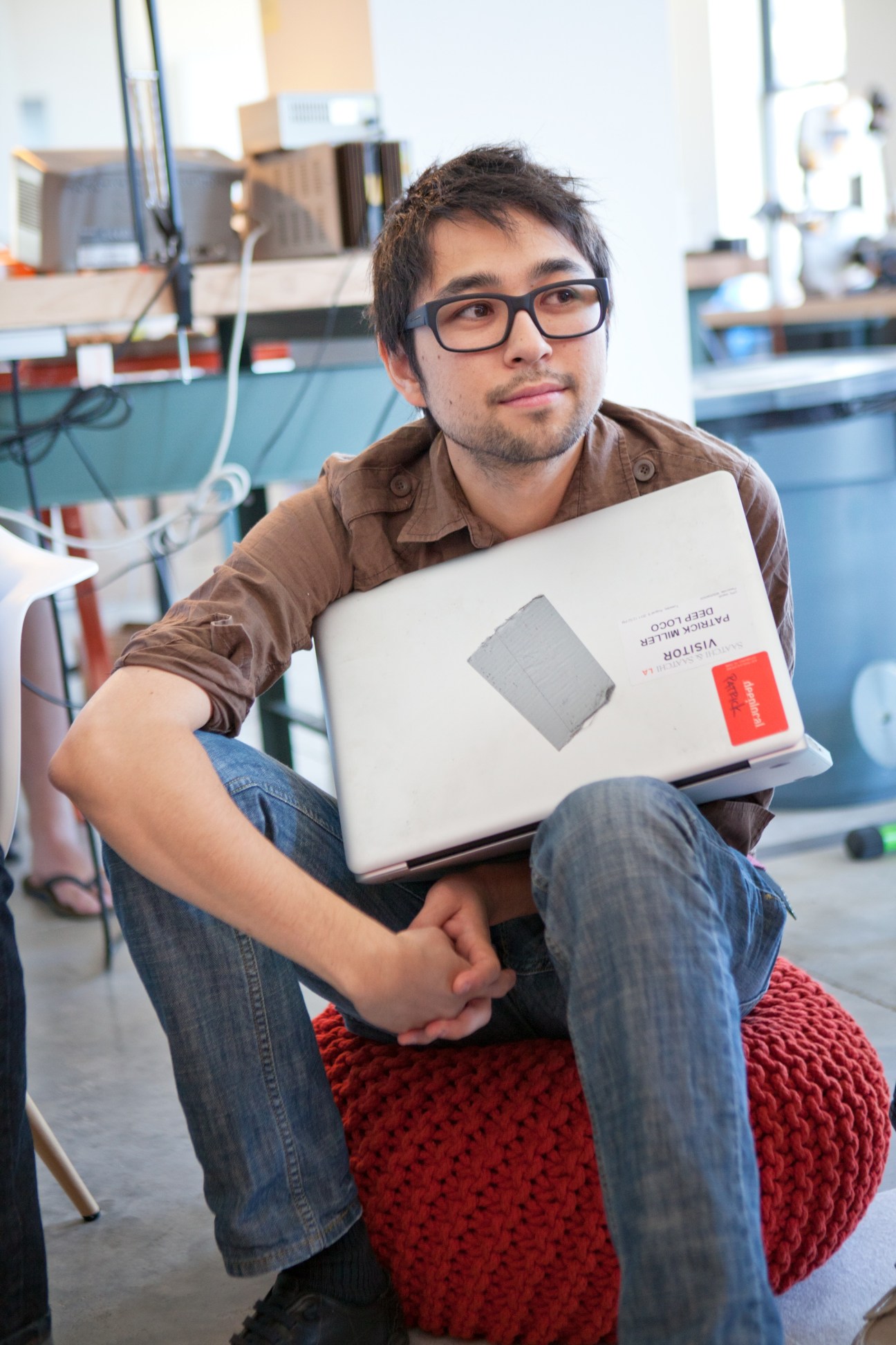 Patrick Miller from Deeplocal sits in a tech workspace holding a laptop.