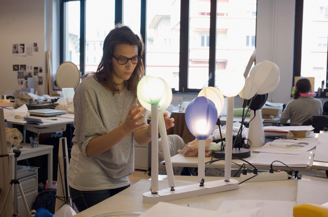 A student examines illuminated lamp prototypes at a workshop desk in ECAL's design studio.