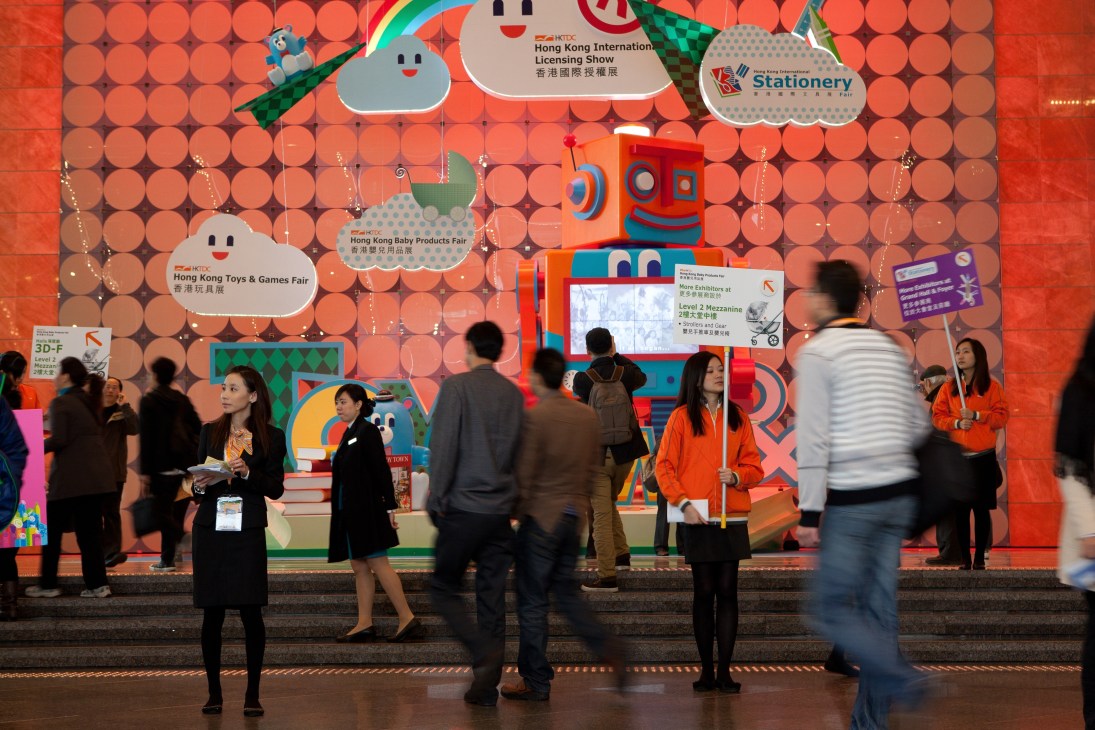 Visitors walk past the colorful main entrance to the Hong Kong Toys & Games Fair with a large robot mascot.