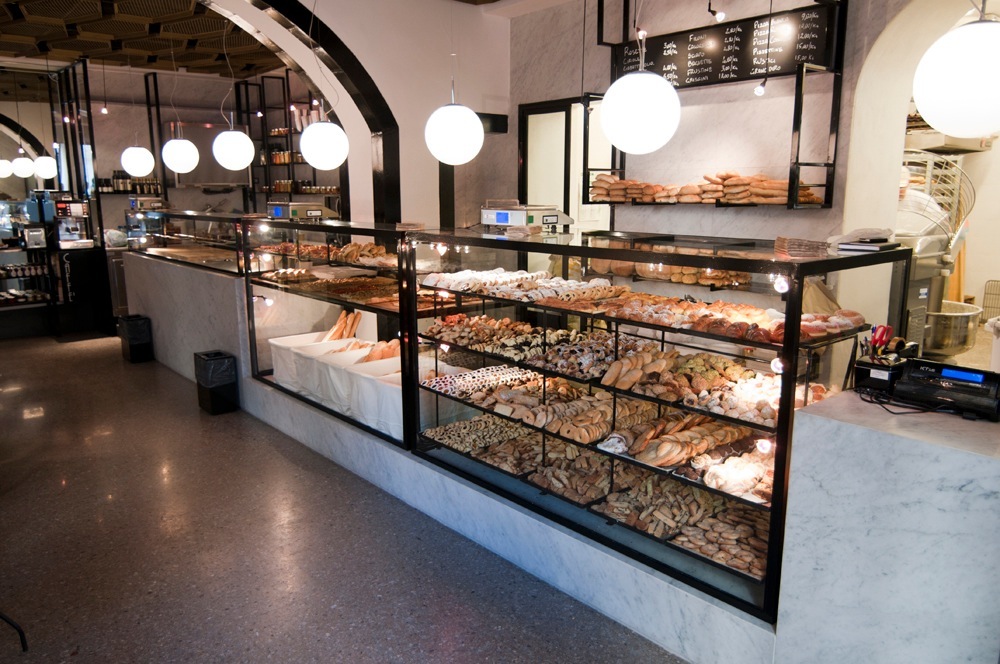 Modern bakery interior with glass display cases of fresh bread and pastries under spherical pendant lights.