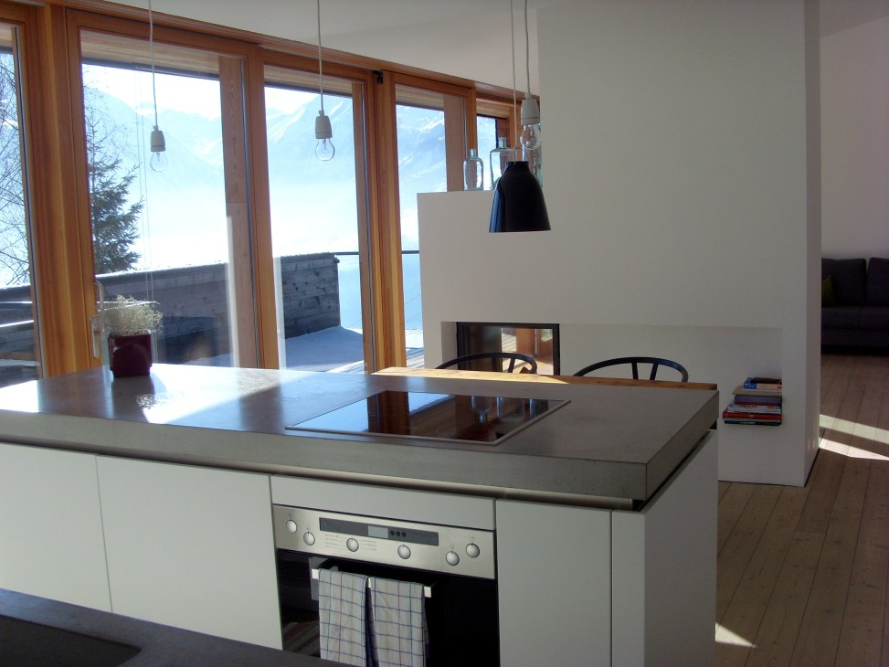 Modern kitchen with island countertop and large windows overlooking Alpine mountains and lake views.