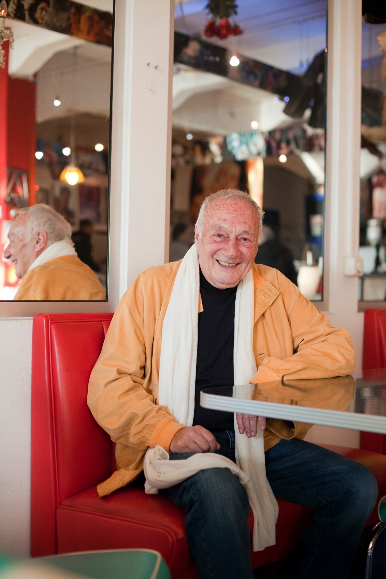 Norbert Gastell, an 81-year-old man in an orange jacket and white scarf, smiles at a Munich café.