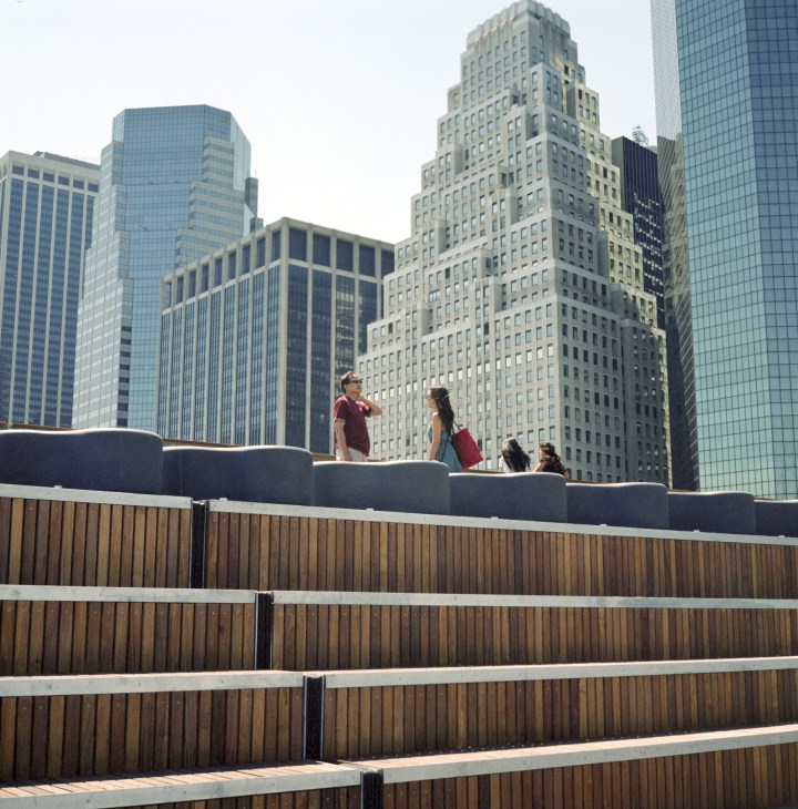 People standing on a wooden deck with metal railings overlooking New York City's skyline of skyscrapers.
