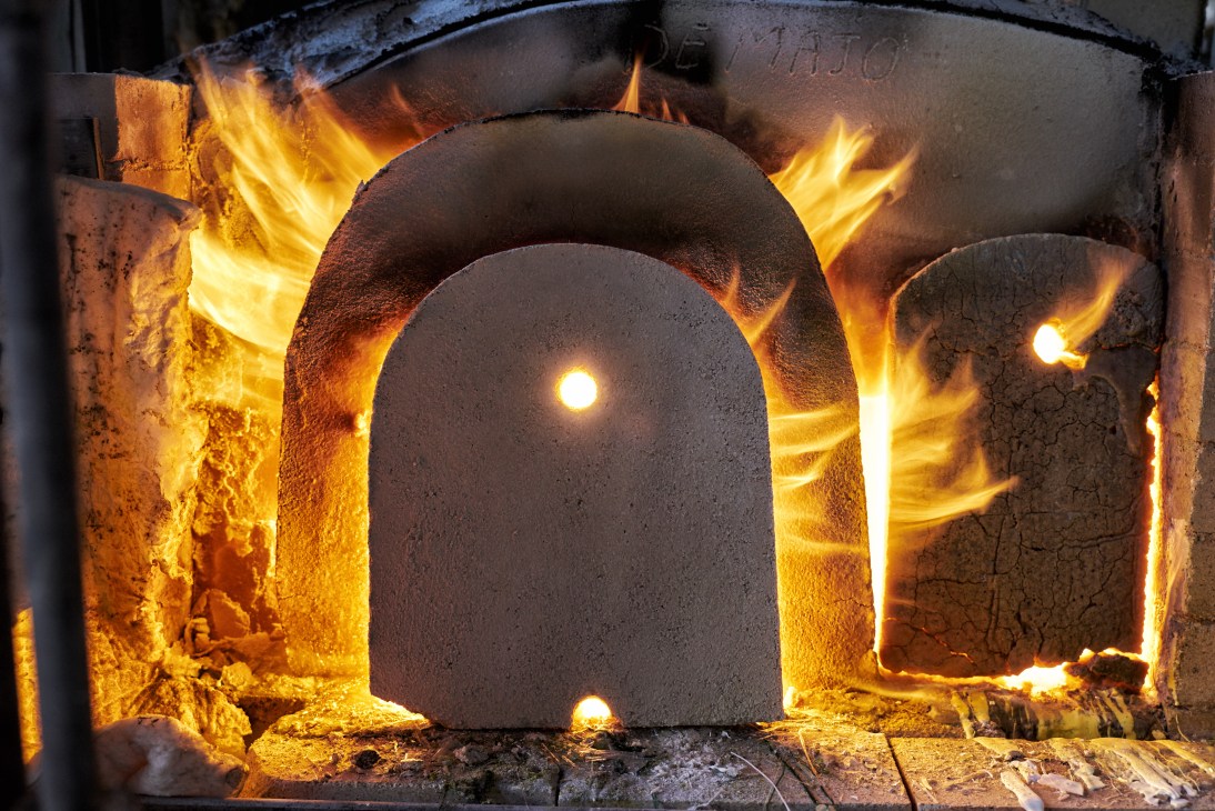 A glass-blowing furnace glowing with intense heat and bright flames surrounding a dark arched opening.