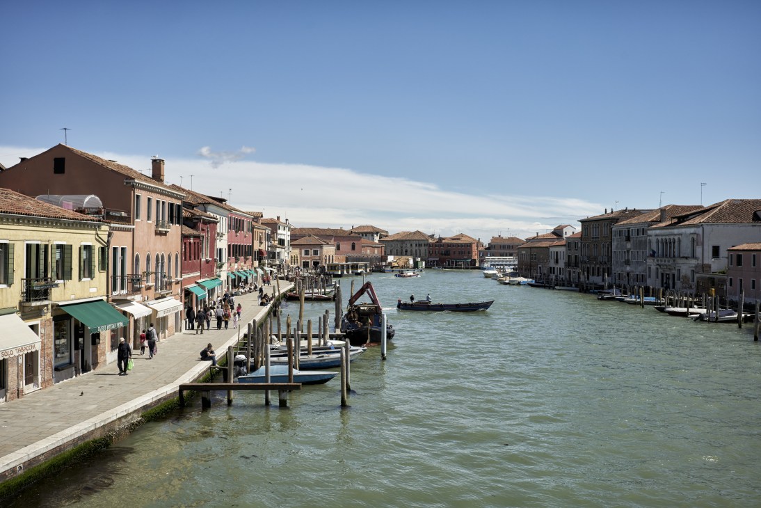 Colorful buildings line a Venetian canal with gondolas and boats on the turquoise water.