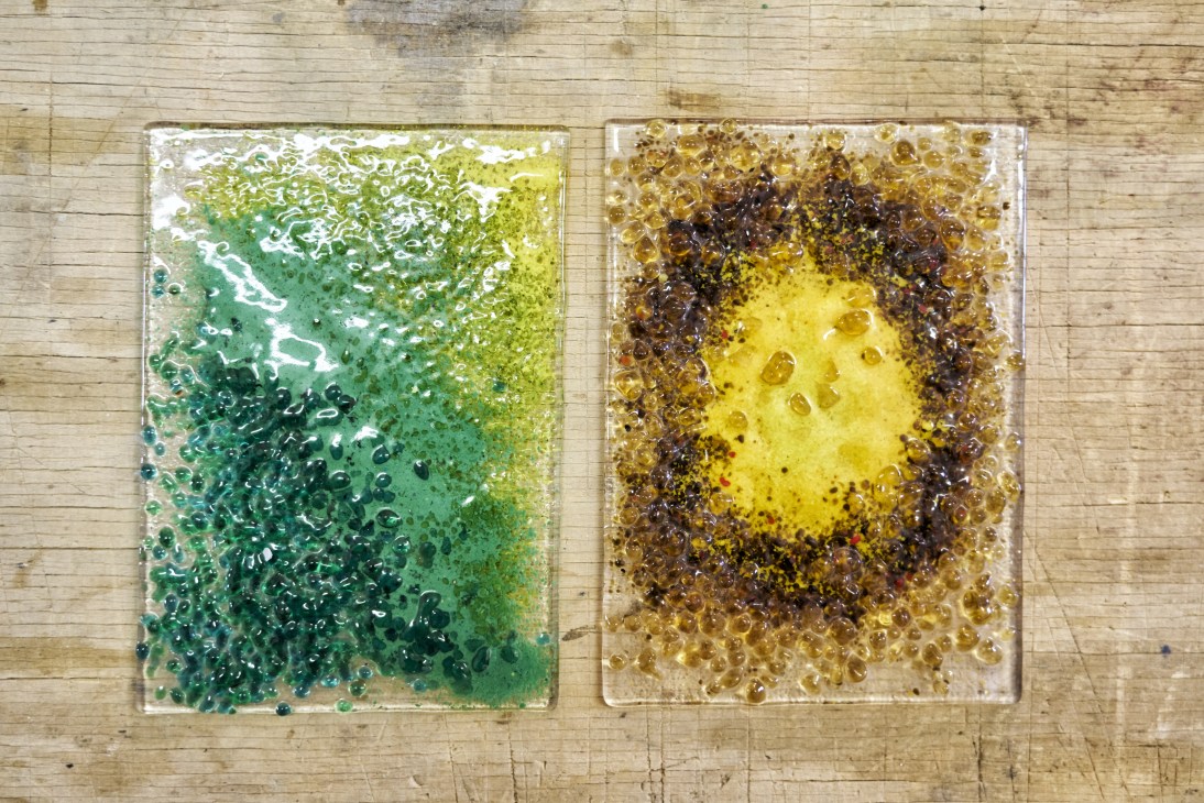 Two glass panels with textured surfaces in green and amber tones on a wooden floor.