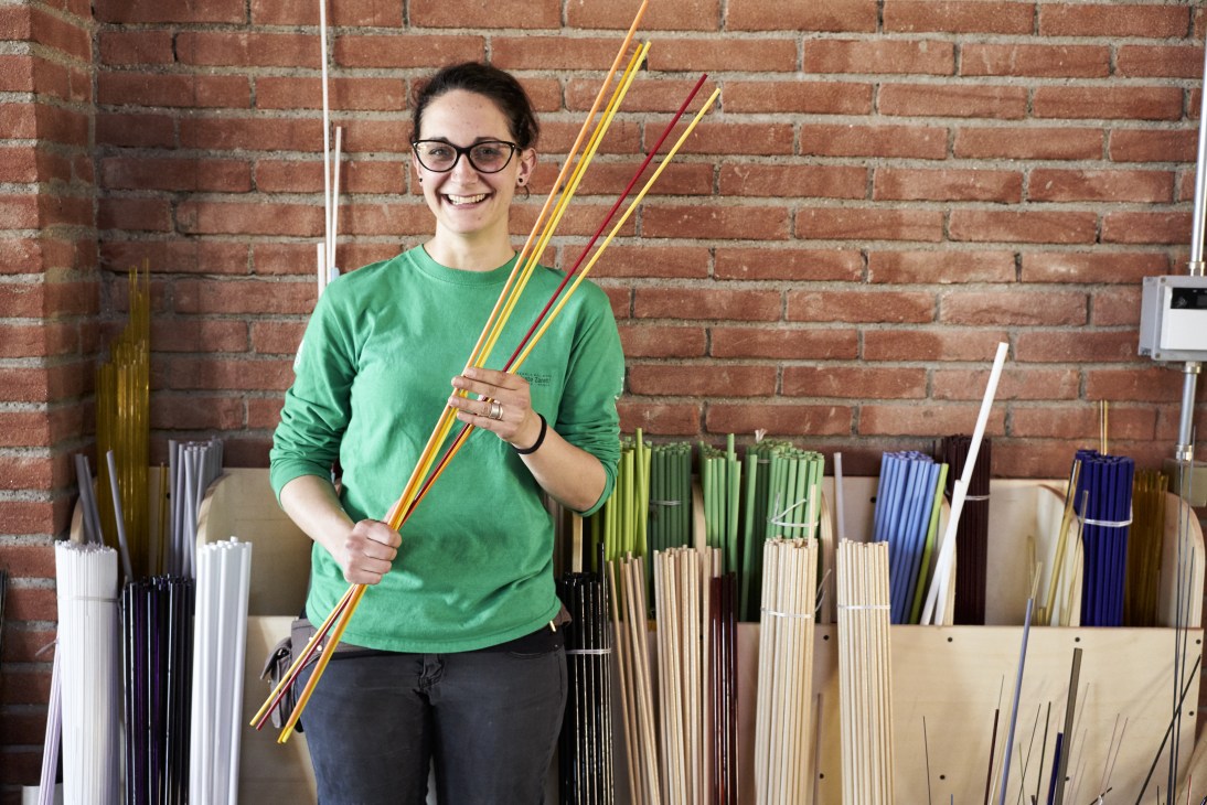 Glass-fusion teacher Elena Menegazzo holding colored glass rods in front of a brick wall.