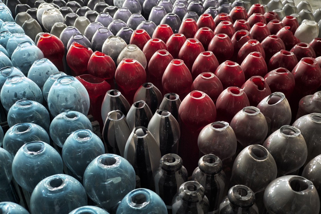 Colorful glass vases in blue, red, black and cream arranged in rows awaiting polishing.