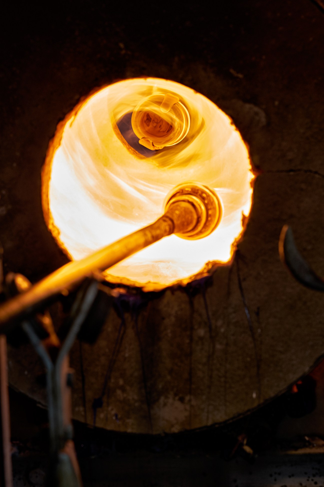 Glowing molten glass being shaped on a steel rod in a furnace at high temperature.