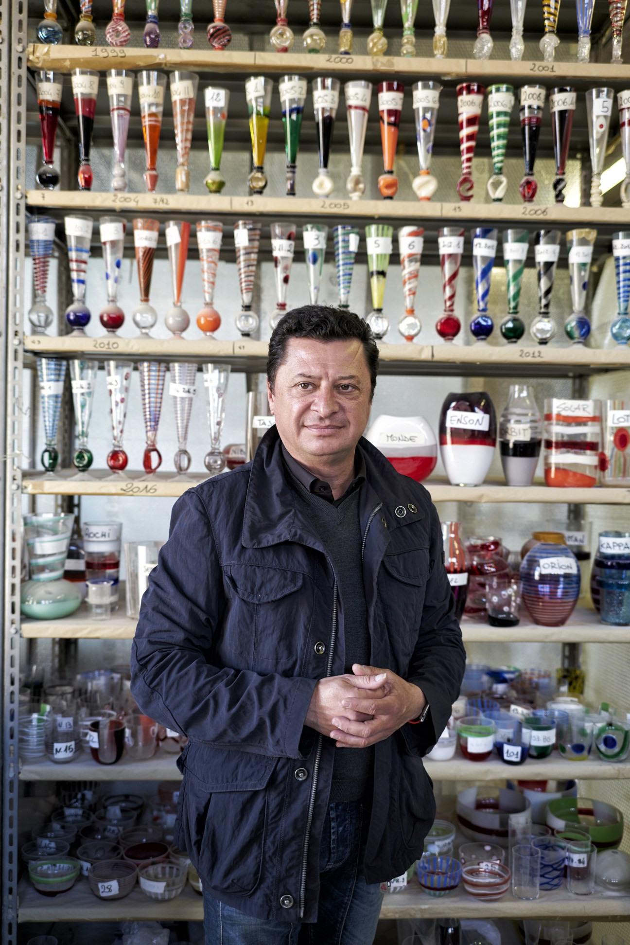 Antonio Ceschel, general manager at Carlo Moretti, stands before shelves of colorful glass vessels and samples.
